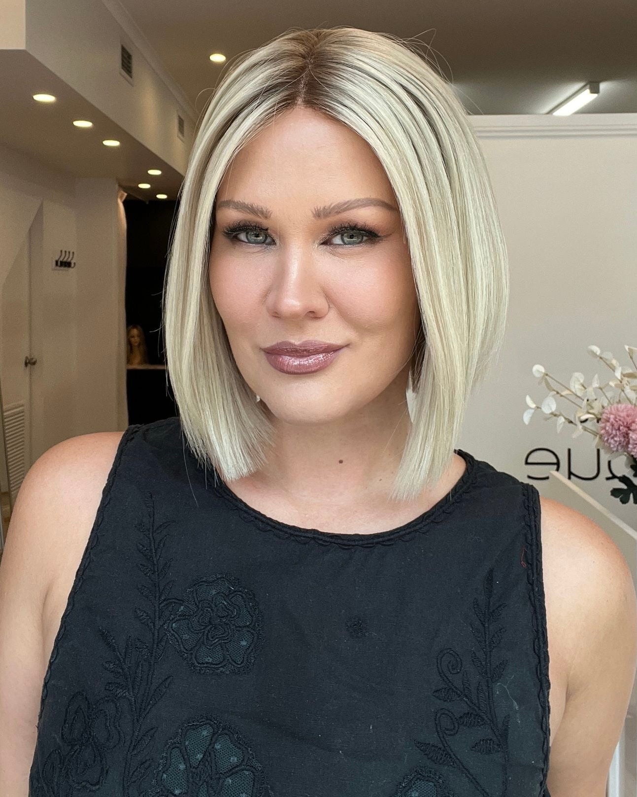 A woman showcasing a 12-inch platinum blonde bob wig with a lace front and a silicone grip cap.