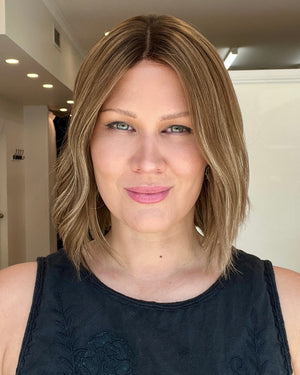 A person wearing a 12 inch straight Remy human hair wig with a medium ash brown balayage and roots, platinum lace collection.