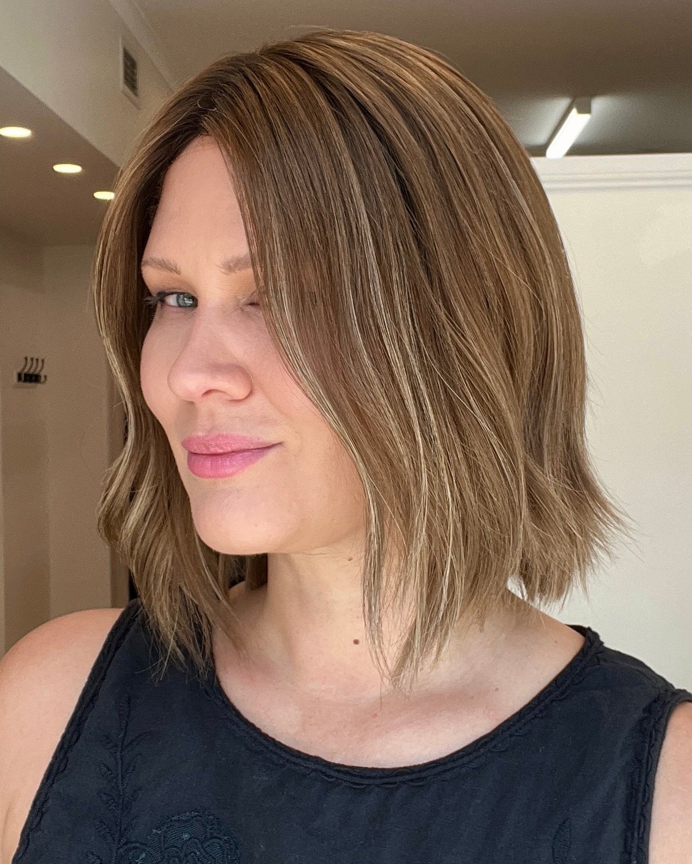 A person wearing a 12 inch straight Remy human hair wig with a medium ash brown balayage and roots, platinum lace collection.