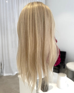 Blonde topper on a mannequin head against a white curtain background