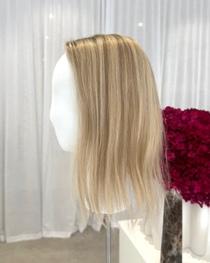 Blonde topper on a mannequin head with a white curtain background