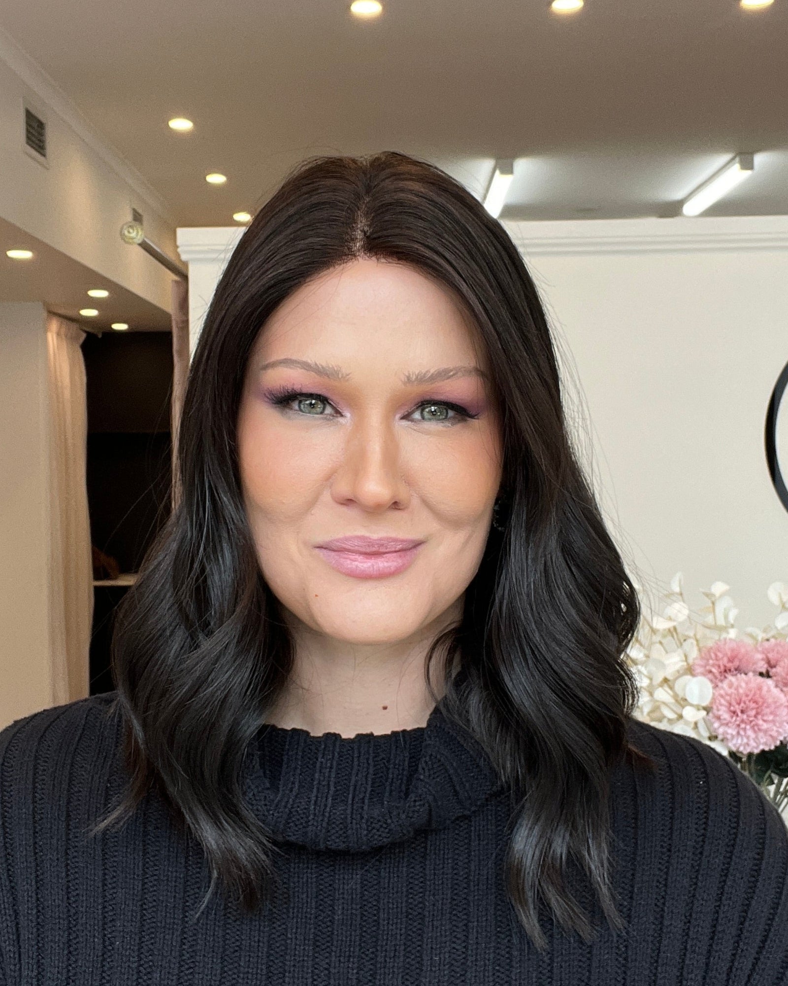Woman in a dark sweater standing in a room with a decorative wall sign.