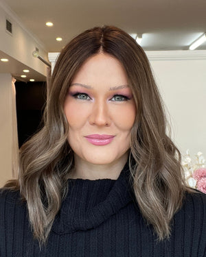 Woman in a dark sweater standing in a room with a decorative wall and flowers.