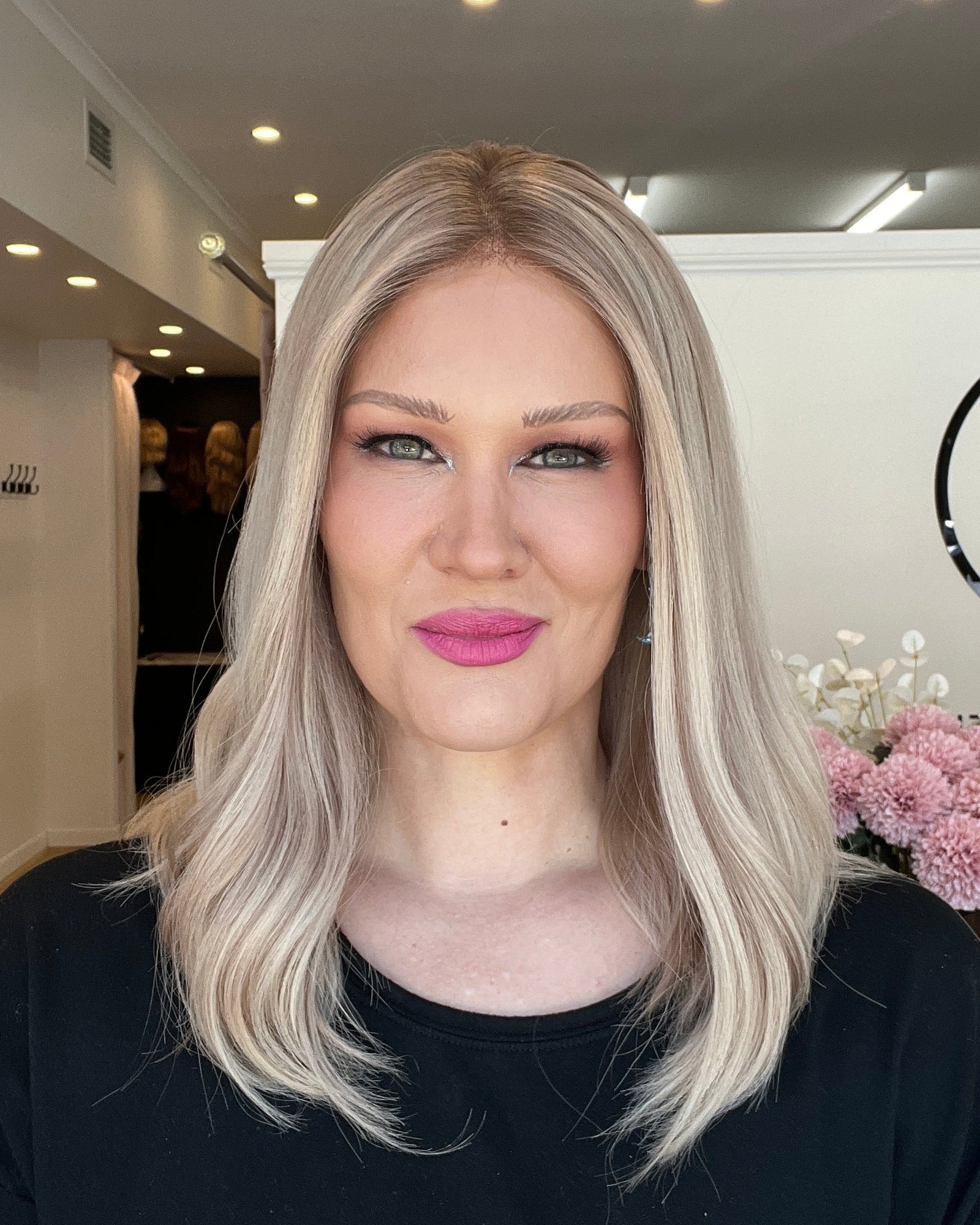 Woman with blonde hair and pink lipstick standing indoors, wearing a black top.