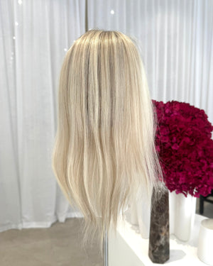 Blonde topper on a mannequin head with a white curtain and red flowers in the background