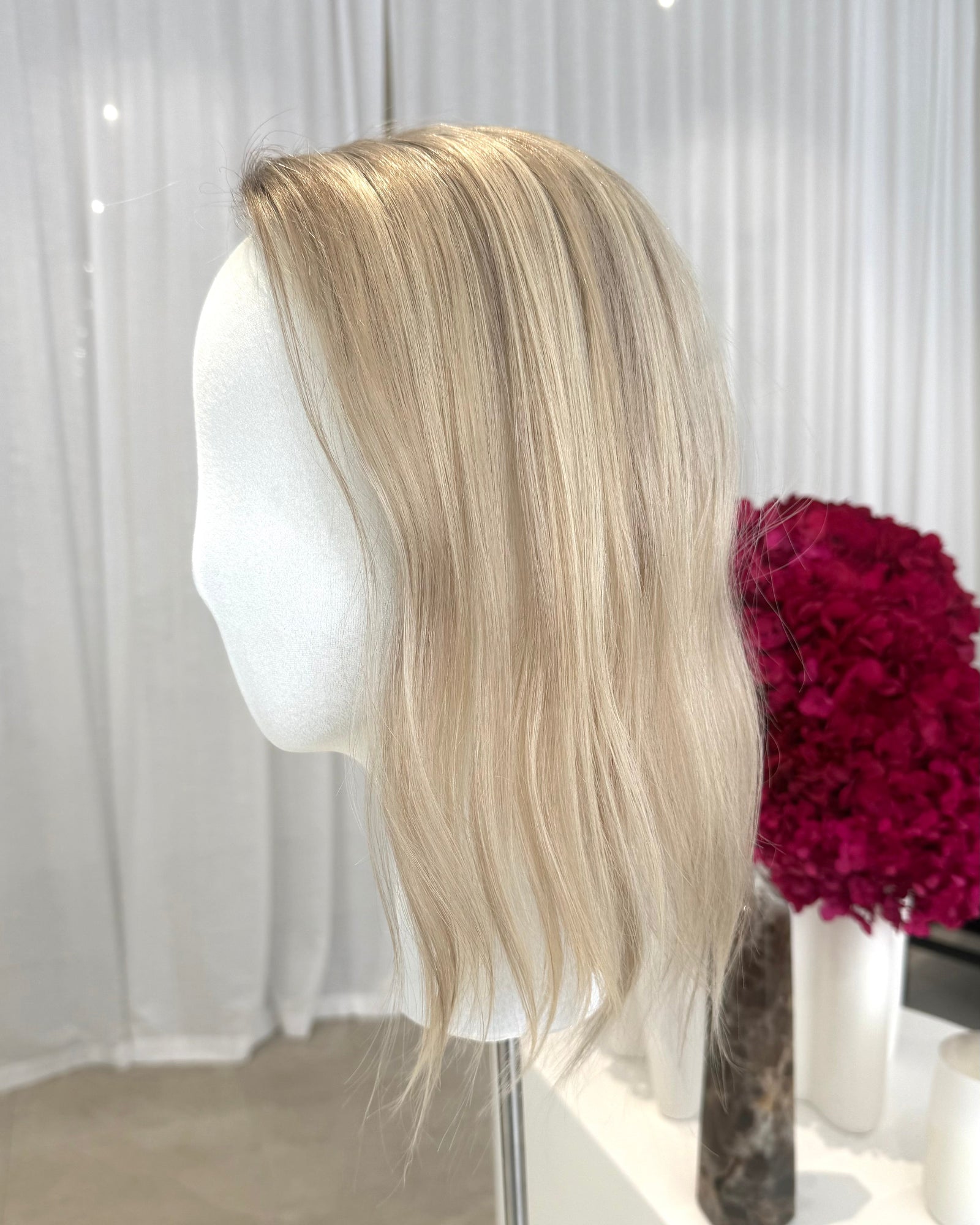 Blonde topper on a mannequin head with a white curtain background