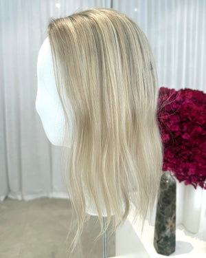 Blonde topper on a mannequin head with a white curtain and pink flowers in the background
