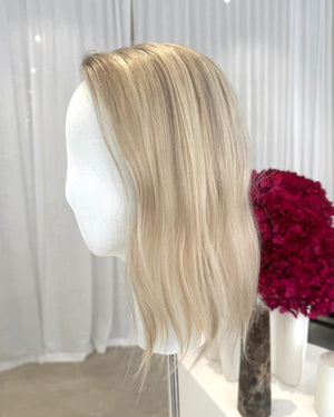 Blonde topper on a mannequin head with a white curtain background