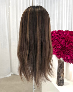 Brown topper on a mannequin head with a white curtain and pink flowers in the background