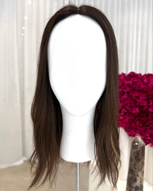 Brown topper on a mannequin head with a white curtain and pink flowers in the background