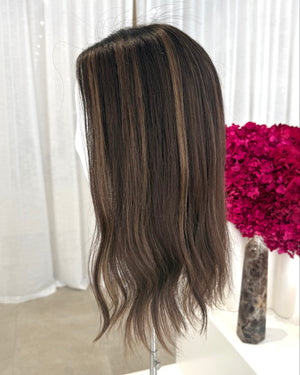 Brown topper on a mannequin head with a white curtain and pink flowers in the background