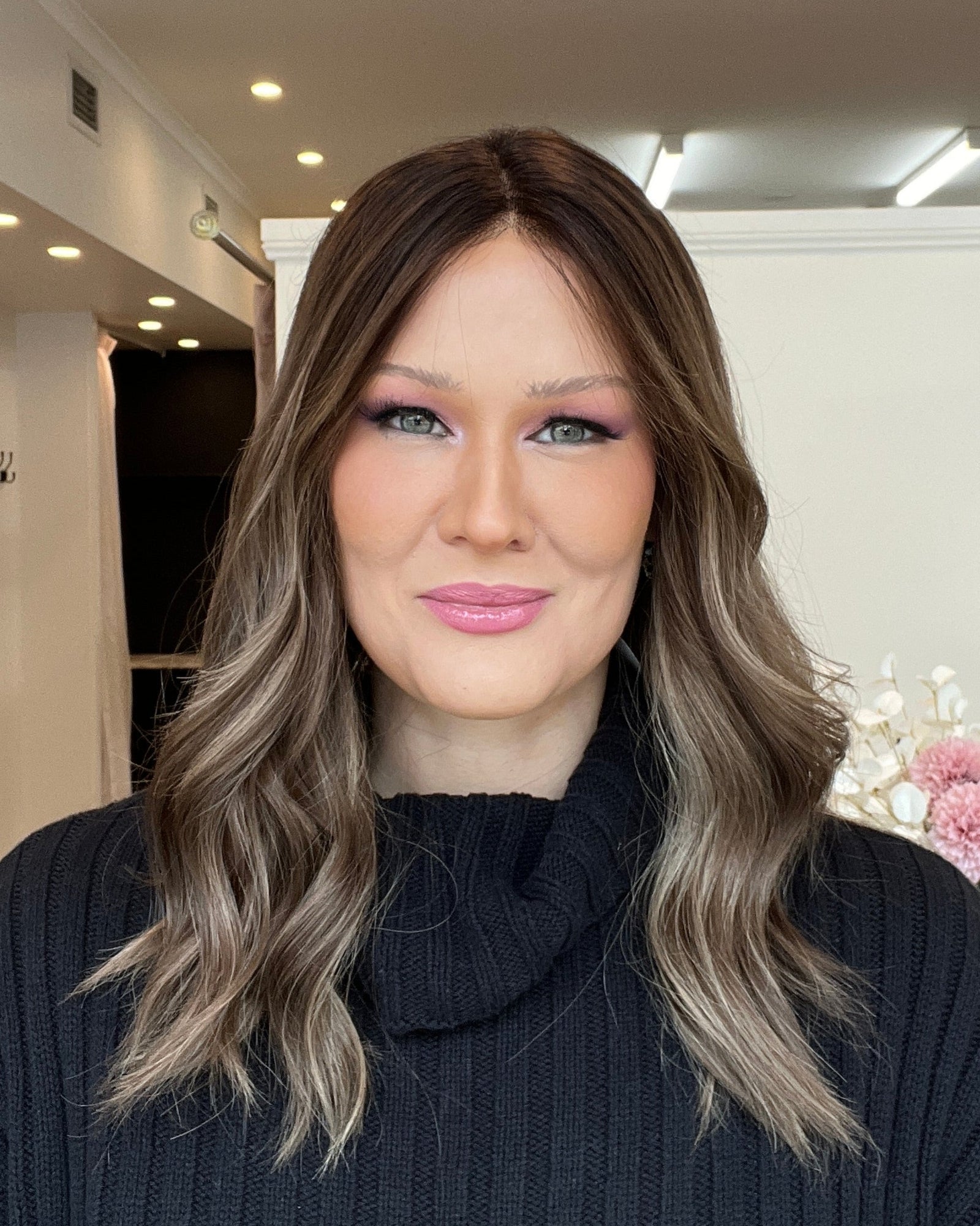 Woman with long hair and makeup standing indoors, looking at the camera.