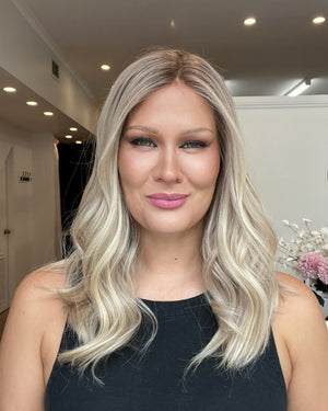 Woman with long blonde hair in a room with white walls and a decorative plant.