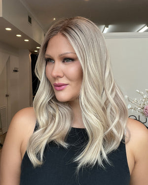Woman with long blonde hair in a room with white walls and a decorative plant.