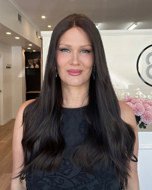 Woman with long dark hair standing indoors, wearing a black top.