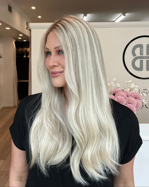 Woman with long blonde hair in a salon setting, looking at herself in the mirror.