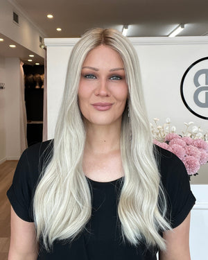 Woman with long blonde hair standing in a room with a logo on the wall.