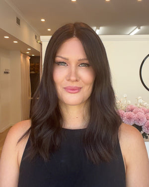 Woman with long dark hair standing indoors with a decorative wall in the background