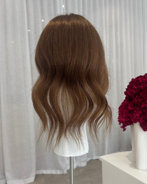 Brown topper on a mannequin head with a white curtain and red flowers in the background