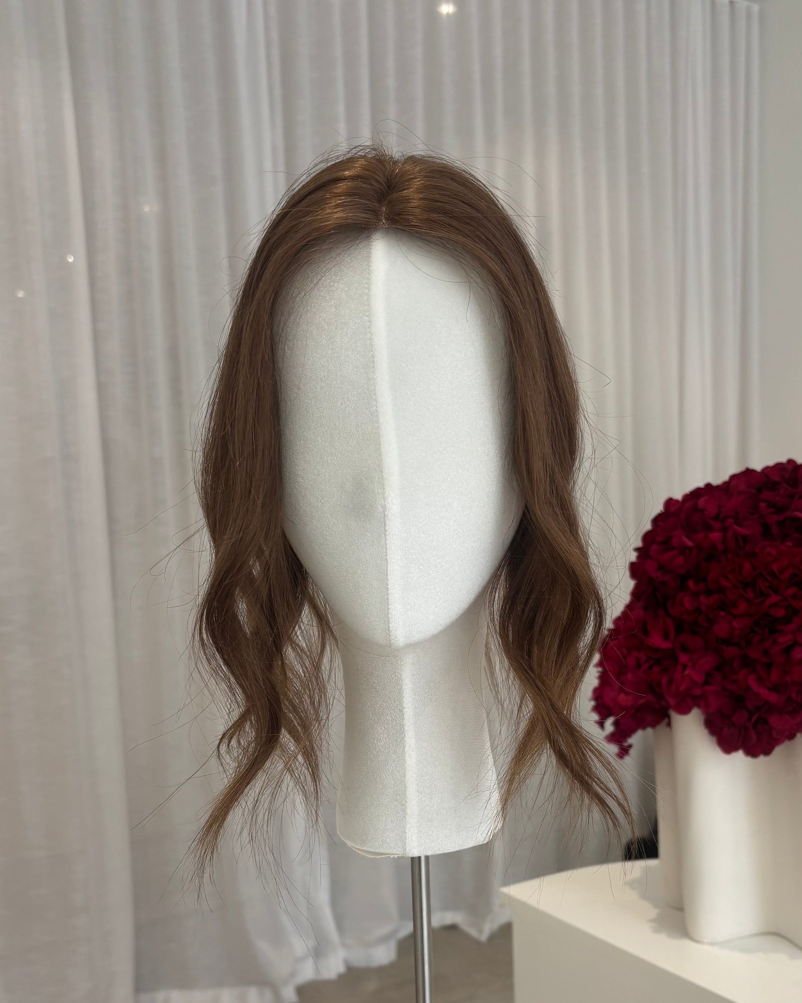 Brown topper on a mannequin head with a white curtain and red flowers in the background