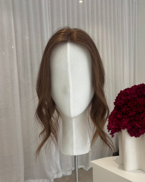 Brown topper on a mannequin head with a white curtain background