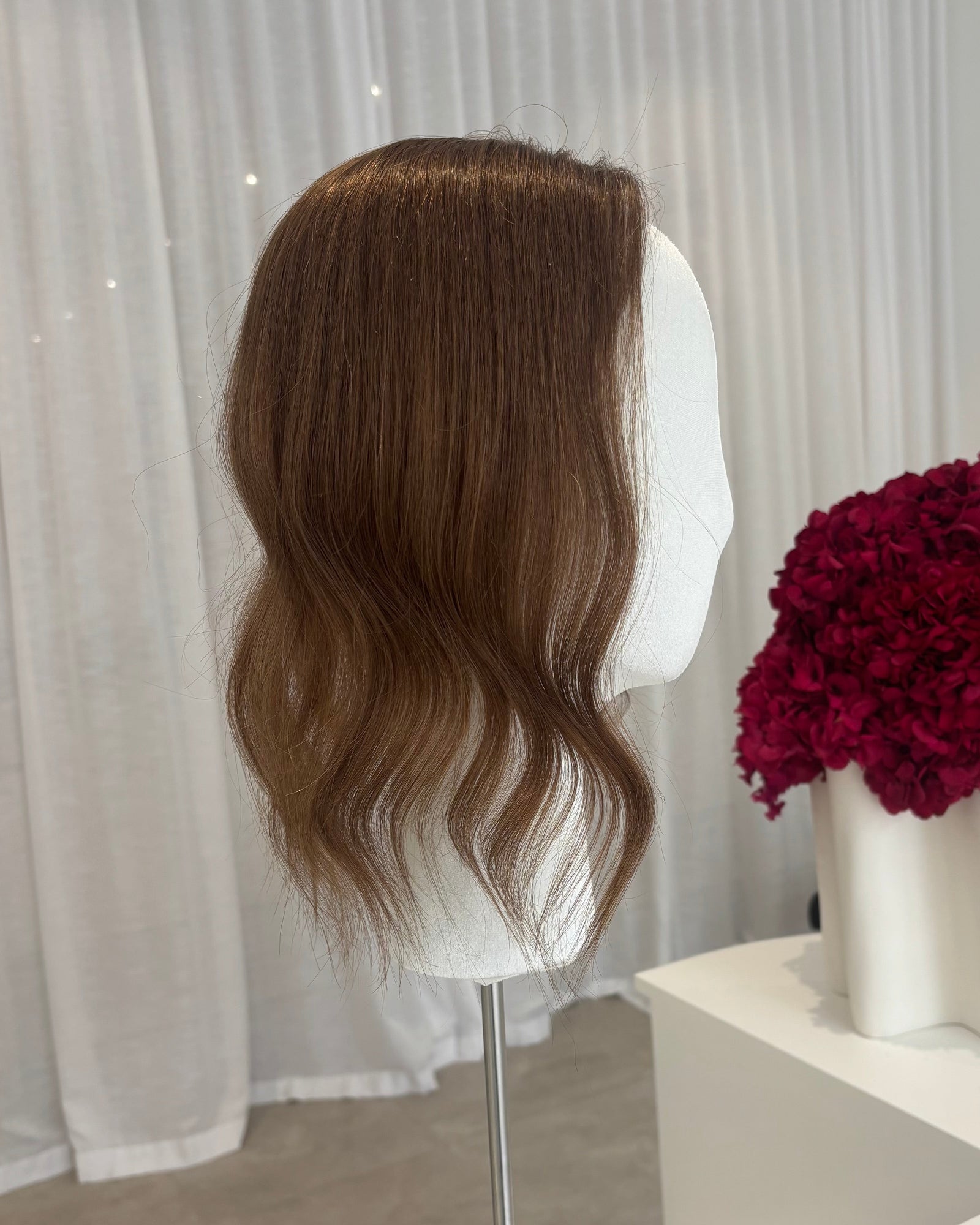 Brown topper on a mannequin head with a white curtain and red flowers in the background