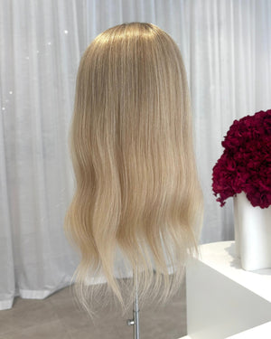 Blonde topper on a mannequin head with a white curtain and red flowers in the background