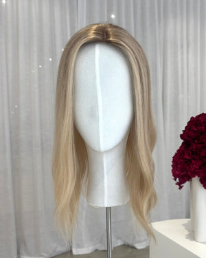 Blonde topper on a mannequin head with a white curtain and red flowers in the background