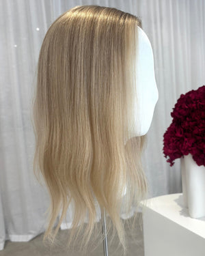 Blonde topper on a mannequin head with a white curtain and red flowers in the background