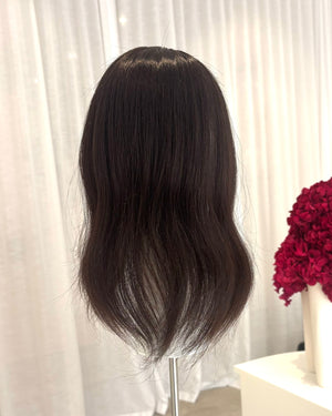 Black topper on a mannequin head with a white curtain and red flowers in the background