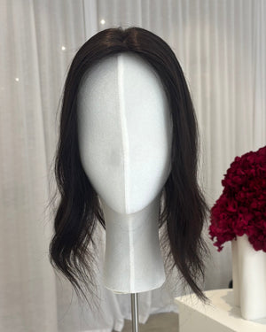Black topper on a mannequin head with a white curtain and red flowers in the background