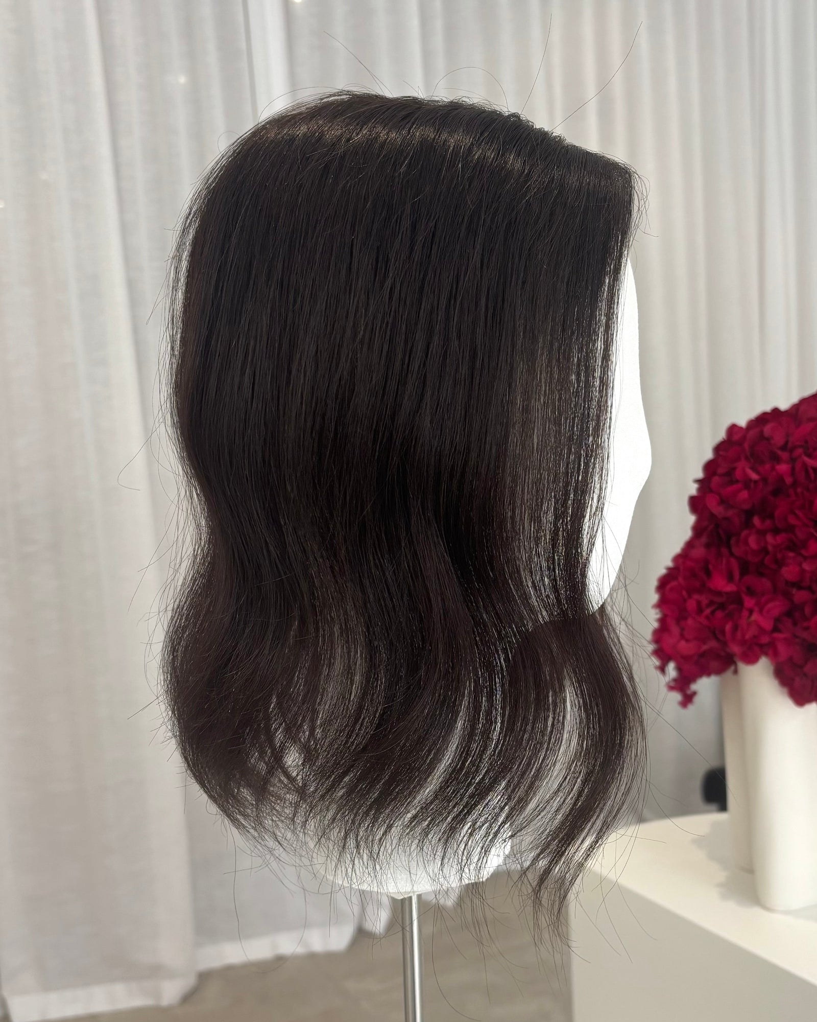 Black topper on a mannequin head with a white curtain and red flowers in the background