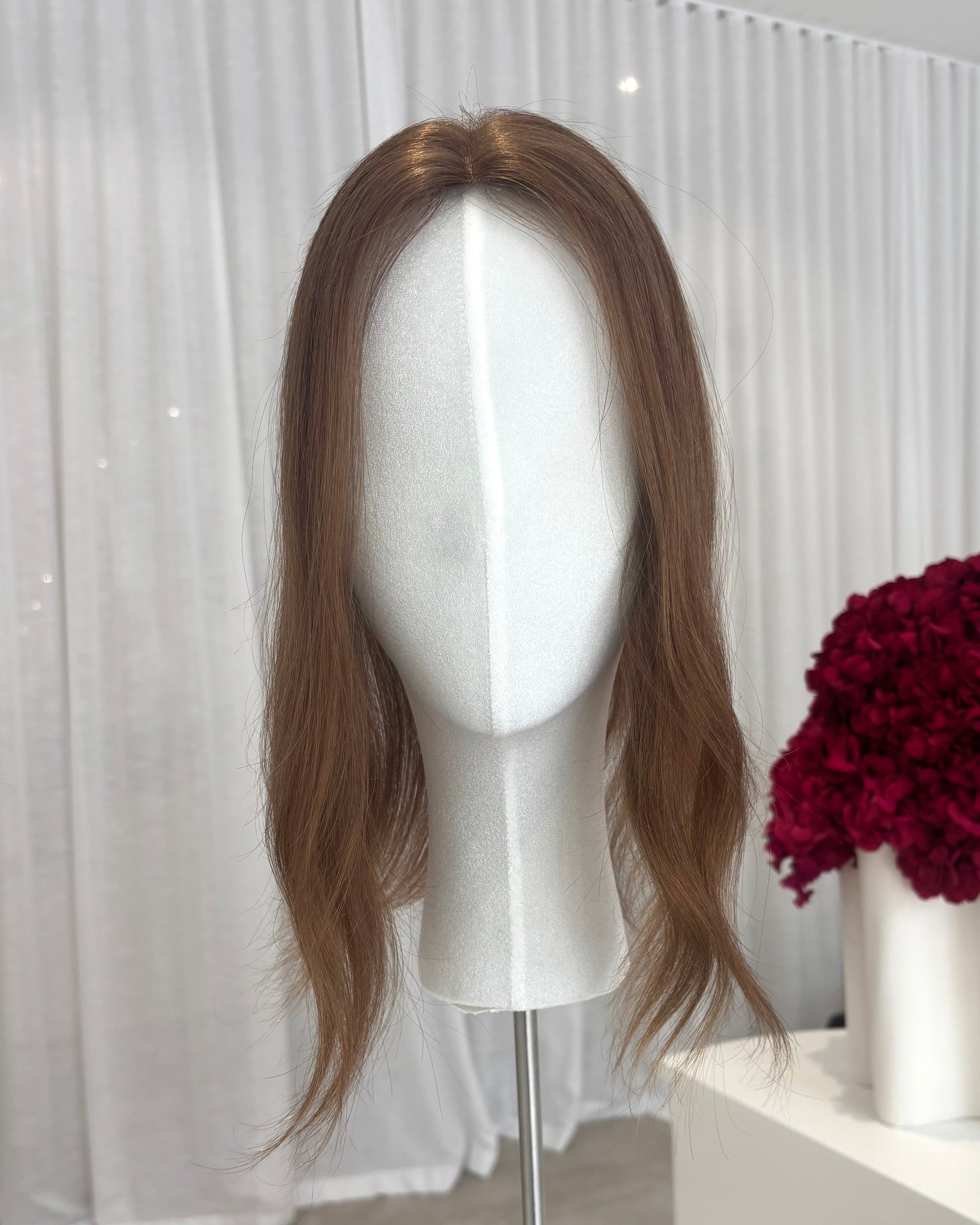 Brown topper on a mannequin head with a white curtain and red flowers in the background