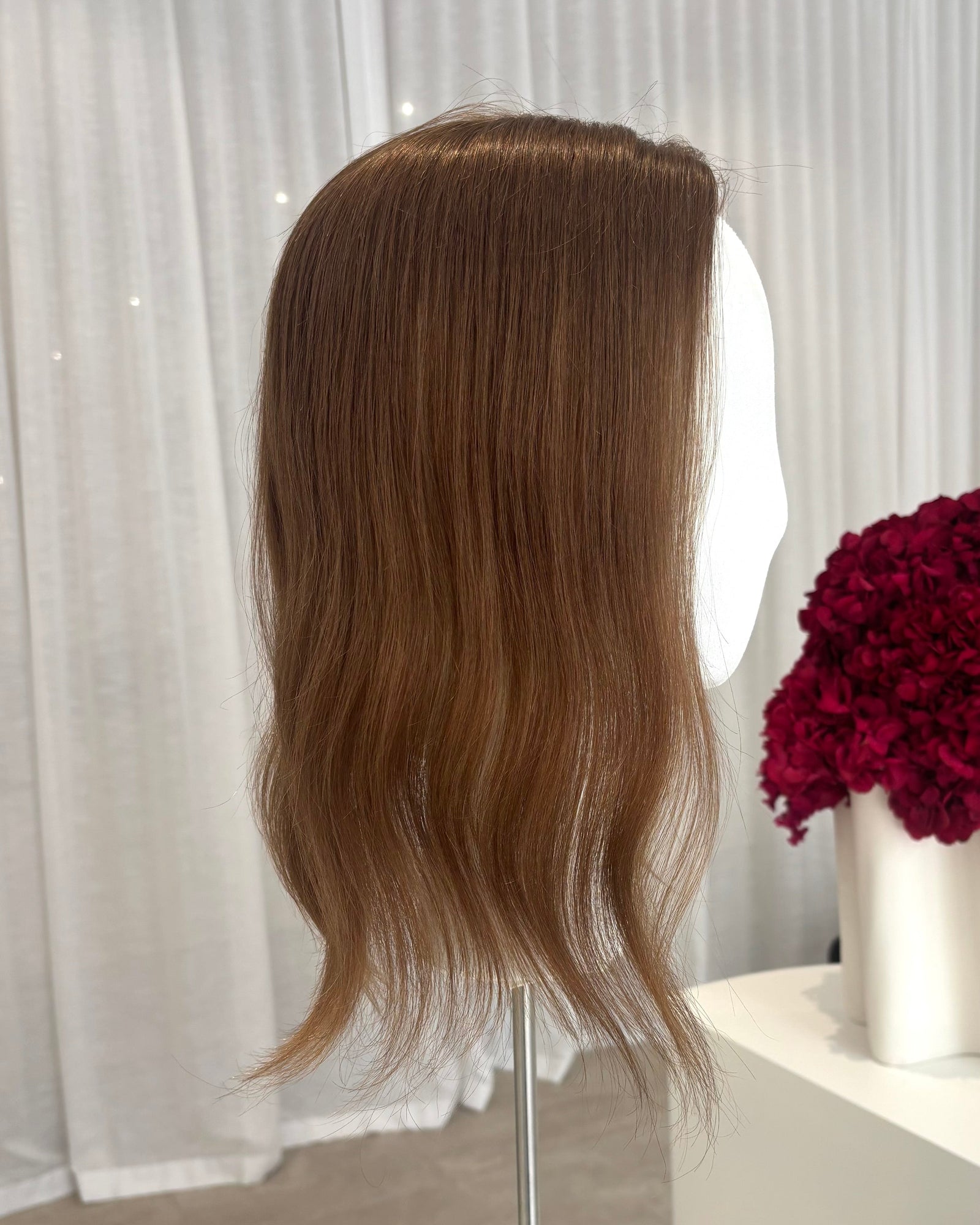 Brown topper on a mannequin head with a white curtain and red flowers in the background