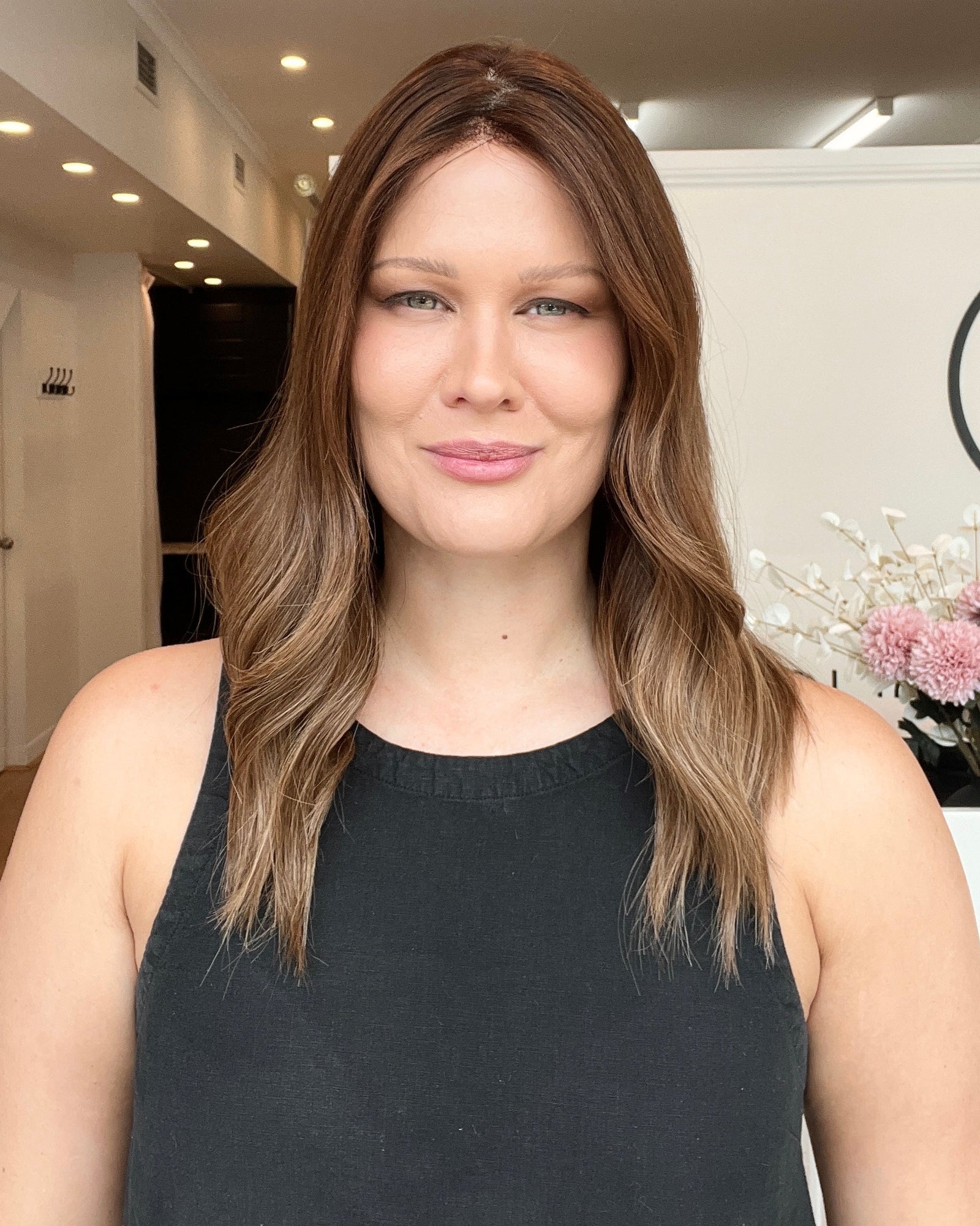 A woman showcasing an 18 inch premium remy human hair wig with ultra light density and a lace front. The wig has a medium brown color with balayage highlights and darker brown roots.