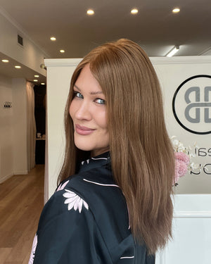 Woman with styled hair in a salon setting with a brand logo in the background