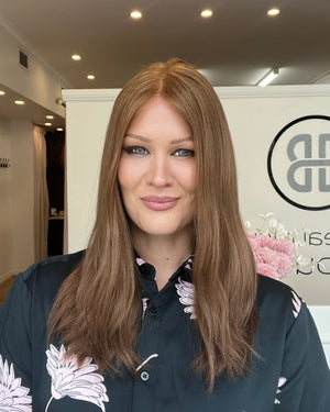 Woman with long reddish brown hair wearing a black floral blouse in an indoor setting.
