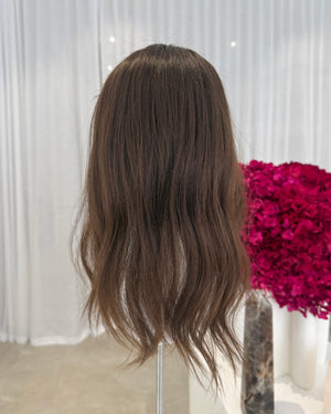 Brown hair topper on a mannequin head with pink flowers in the background