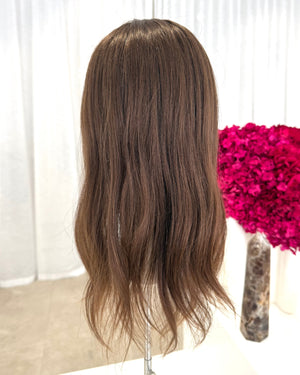 Brown topper on a mannequin head with a blurred pink floral arrangement in the background