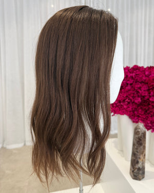 Brown hair topper on a white surface with a pink floral arrangement in the background.