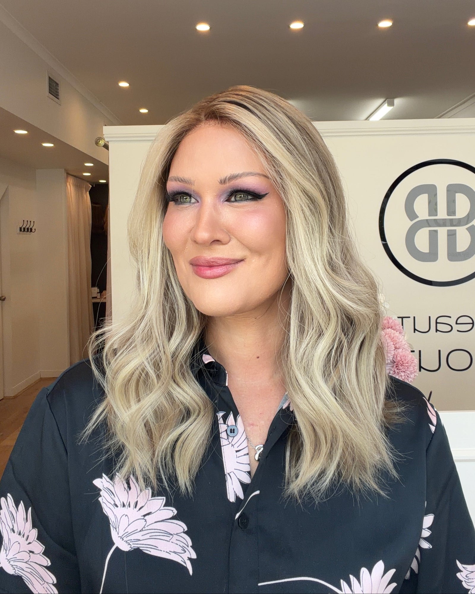 Woman with blonde hair and floral shirt in a room with a logo on the wall
