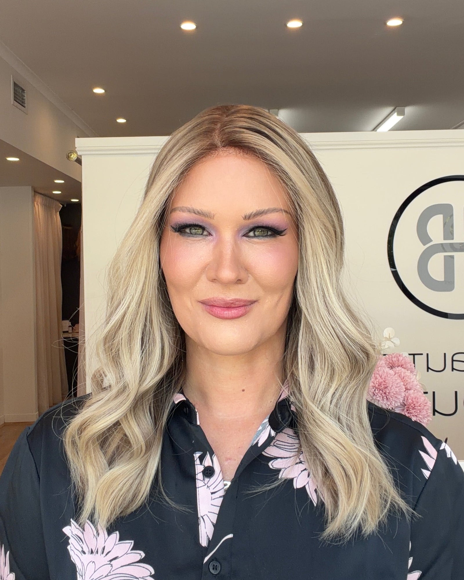 Woman with blonde hair and floral shirt in a room with a logo on the wall