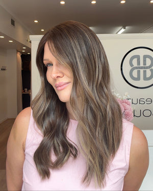 Woman with long, wavy hair in a pink sleeveless top standing in front of a branded wall.