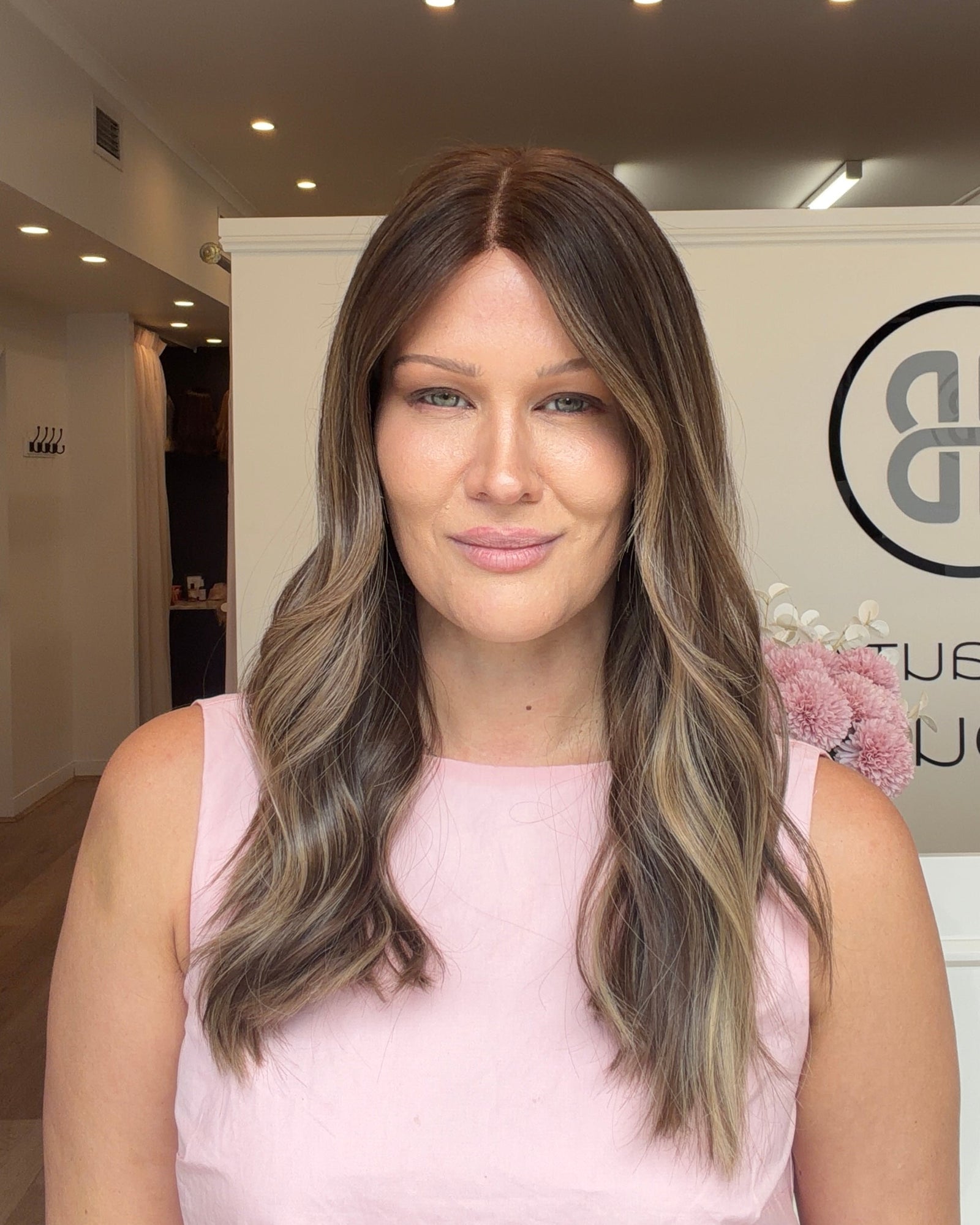 Woman with long, wavy hair in a pink top standing in a modern interior setting.