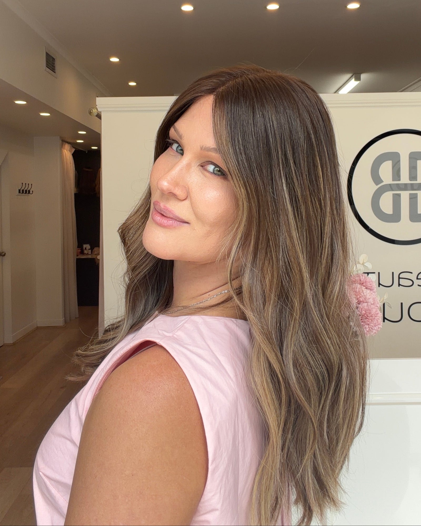 Woman with long, wavy hair in a pink top standing in a modern interior setting.