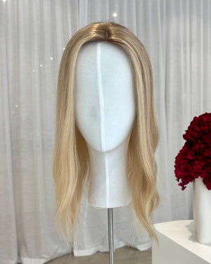 Blonde topper on a mannequin head with a white curtain and red flowers in the background