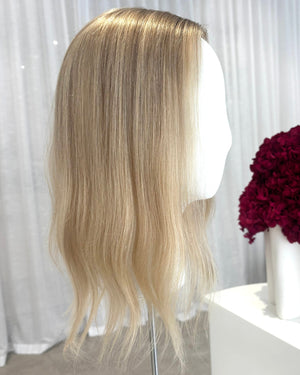 Blonde topper on a mannequin head with a white curtain and red flowers in the background