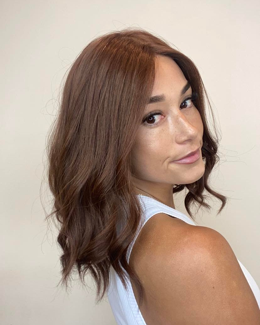 A woman with dark auburn hair, wearing a premium Remy human hair wig that is ultra light and has a silk top with lace front.